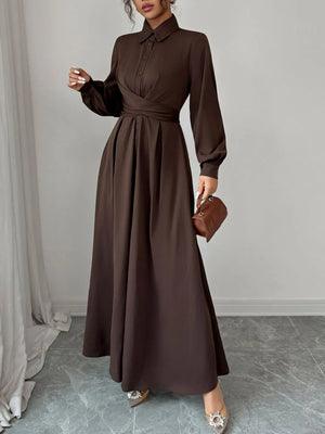 Woman wearing a brown dress holding a matching handbag in a minimalistic setting.