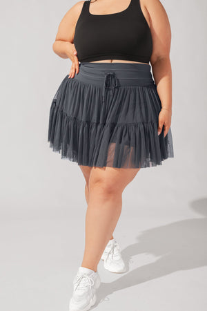 Person wearing a black top and dark gray tiered skirt on a light gray background