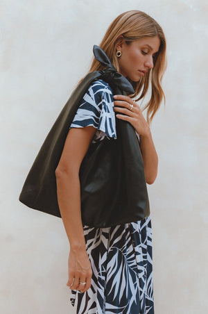 A woman wearing a black knotted leather shoulder bag with a geometric patterned dress.