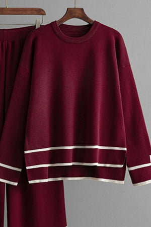 Burgundy sweater with white stripes on a hanger against a gray background