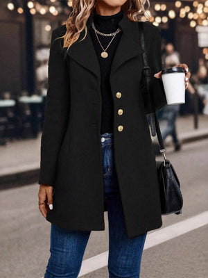 Person wearing a black coat with gold buttons, holding a coffee cup on a street.