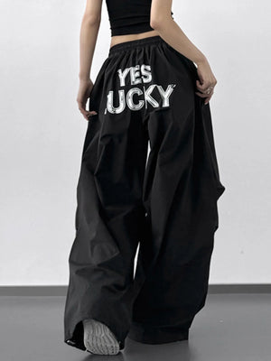 Person wearing black wide-leg pants with 'YES LUCKY' text on a plain background