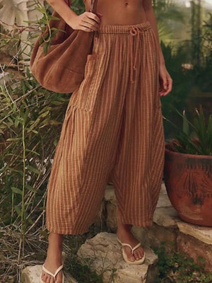 Person wearing brown striped pants and holding a brown bag in an outdoor setting.