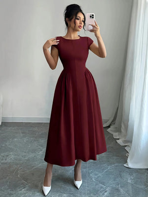 Woman taking a mirror selfie wearing a burgundy dress in a room with white curtains.