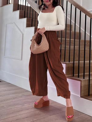 Woman in brown pants and white top holding a woven handbag on a staircase.