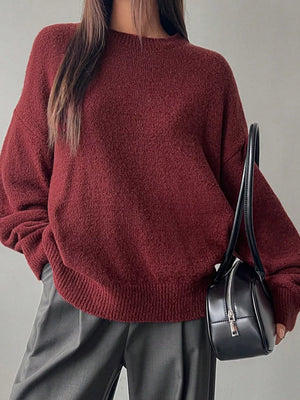 Person wearing a maroon sweater holding a black handbag against a neutral background