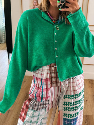Person wearing a green cardigan and plaid pants taking a mirror selfie.