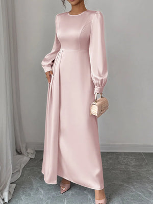 Woman wearing a pink long-sleeve dress holding a matching handbag against a gray background