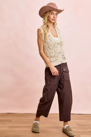 Woman wearing a beige sleeveless top and brown pants with a pink background