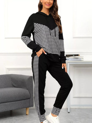 Woman wearing a black and white houndstooth patterned tracksuit in a room with a gray sofa and white wall.
