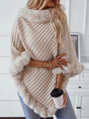 Woman wearing a beige knitted poncho with fur trim, holding a coffee cup.