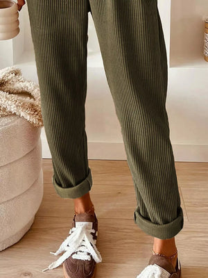 Person wearing green ribbed pants with white sneakers in a home setting