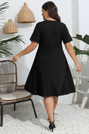 Woman wearing a black dress in an indoor setting with plants and a chair.