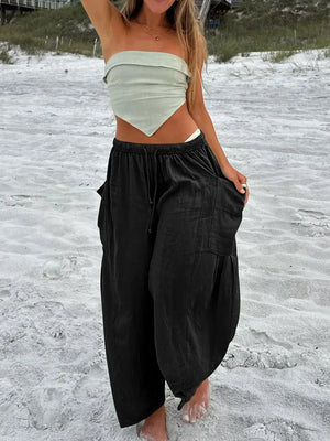 Person wearing a white strapless top and black wide-leg pants on a sandy beach.