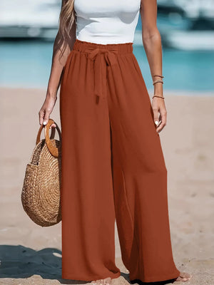 Person wearing rust-colored wide-leg pants on a beach