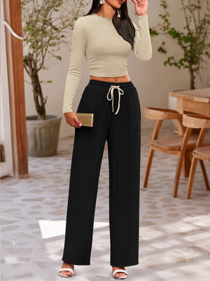 Woman wearing a beige long-sleeve top and black wide-leg pants in an outdoor setting.