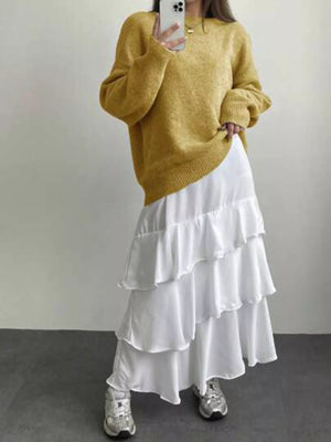 Person wearing a mustard yellow sweater and white ruffled skirt against a plain background