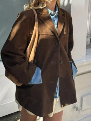 Person wearing a brown coat with blue lining, holding a tan bag indoors.