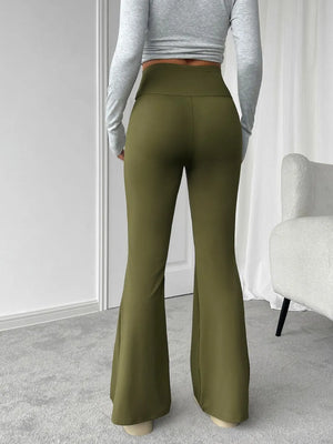 Person wearing olive green flared pants and a gray long-sleeve top in a minimalistic room.