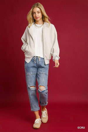 Woman wearing a beige jacket, white shirt, blue jeans, and beige sneakers on a red background