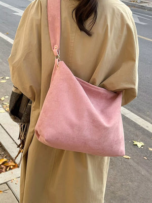 Person wearing a beige coat with a pink shoulder bag on a street.