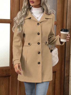 Woman wearing a beige coat holding a coffee cup in front of a wooden door.