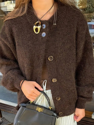 Person wearing a brown cardigan holding a black handbag with a blurred background