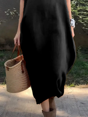Person wearing a black dress holding a woven bag outdoors.