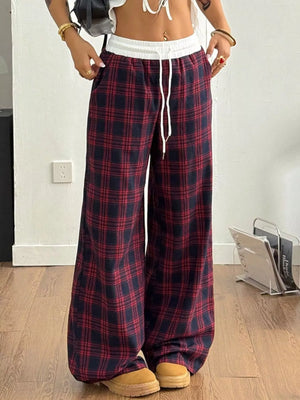 Person wearing red and blue plaid pants with a white top indoors.