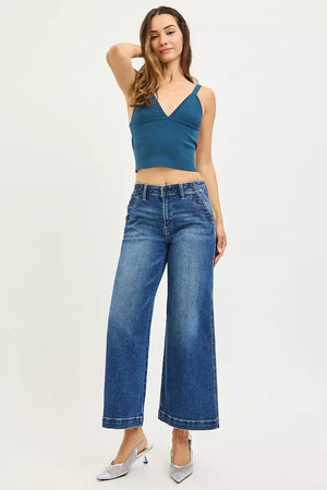 Woman wearing a blue tank top and wide-leg jeans on a white background