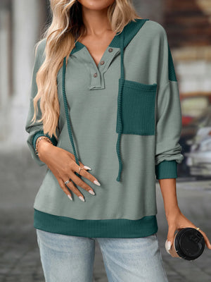 Woman wearing a green and teal sweater holding a coffee cup.