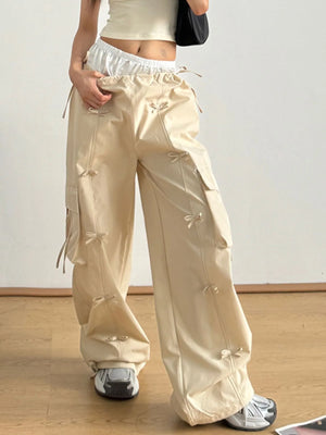 Person wearing beige wide-leg pants with decorative bows on a plain background
