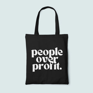Black tote bag with 'people over profit' text on a light blue background
