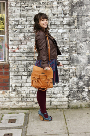 A woman standing by a wall holding Mi Vida Foldover Tote