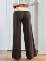 Person wearing brown wide-leg pants with a white top in a minimal indoor setting.