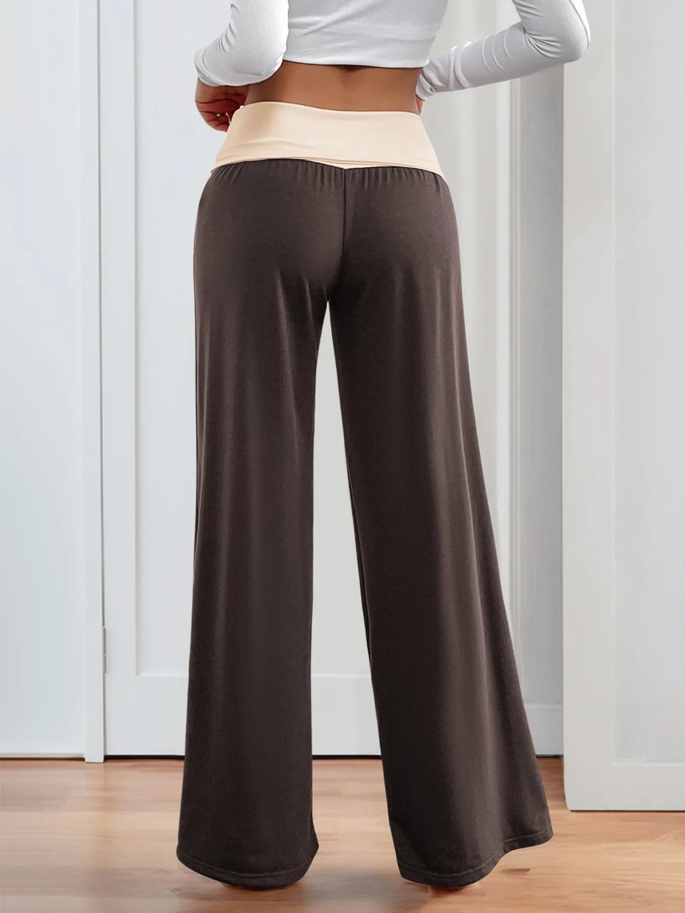 Person wearing brown wide-leg pants with a white top in a minimal indoor setting.