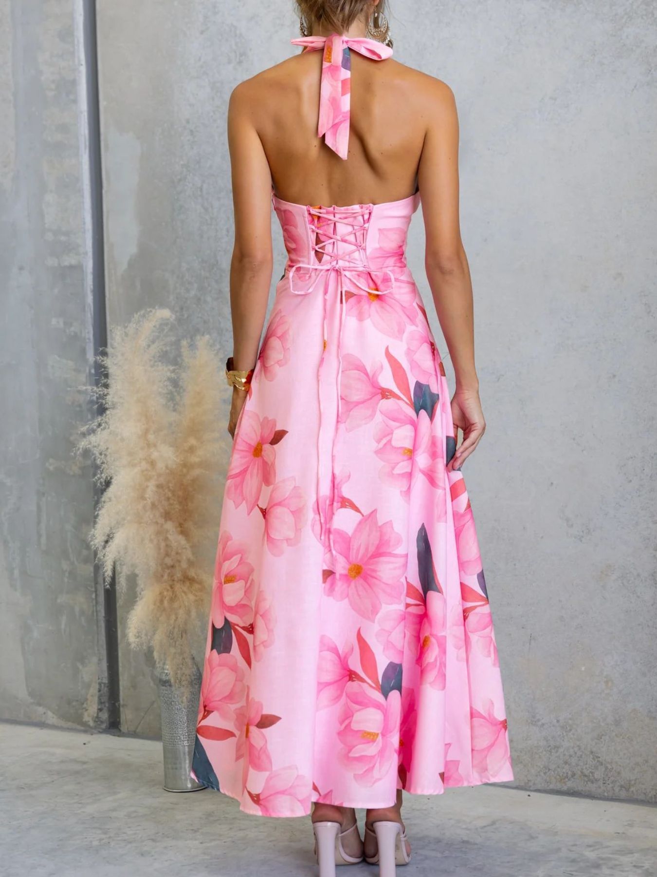 Woman wearing a pink floral dress with a gray wall and potted plant in the background