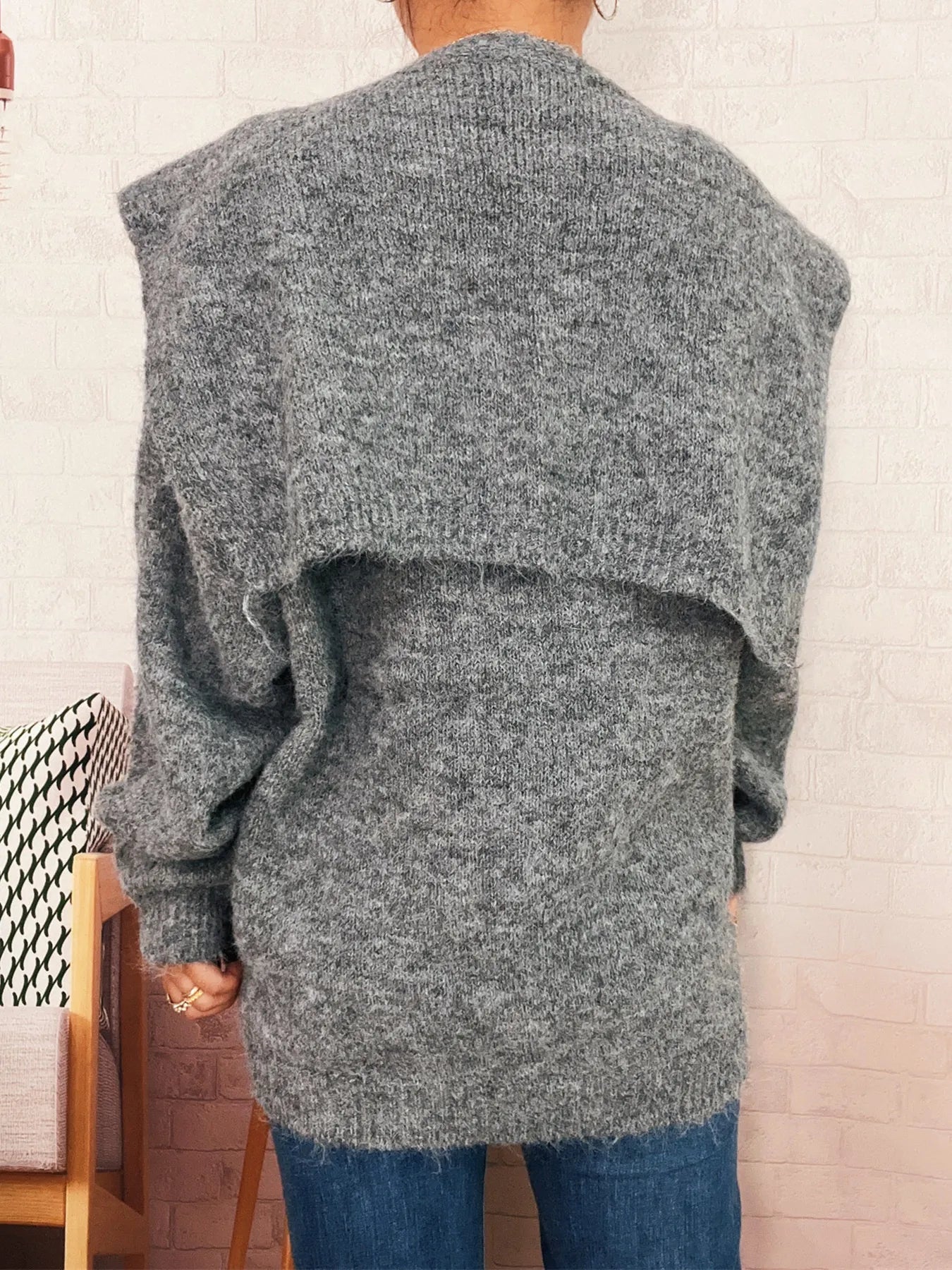 Person wearing a gray oversized sweater with a neutral background