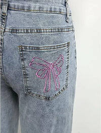 Blue jeans with a pink bow design on the back pocket against a white background
