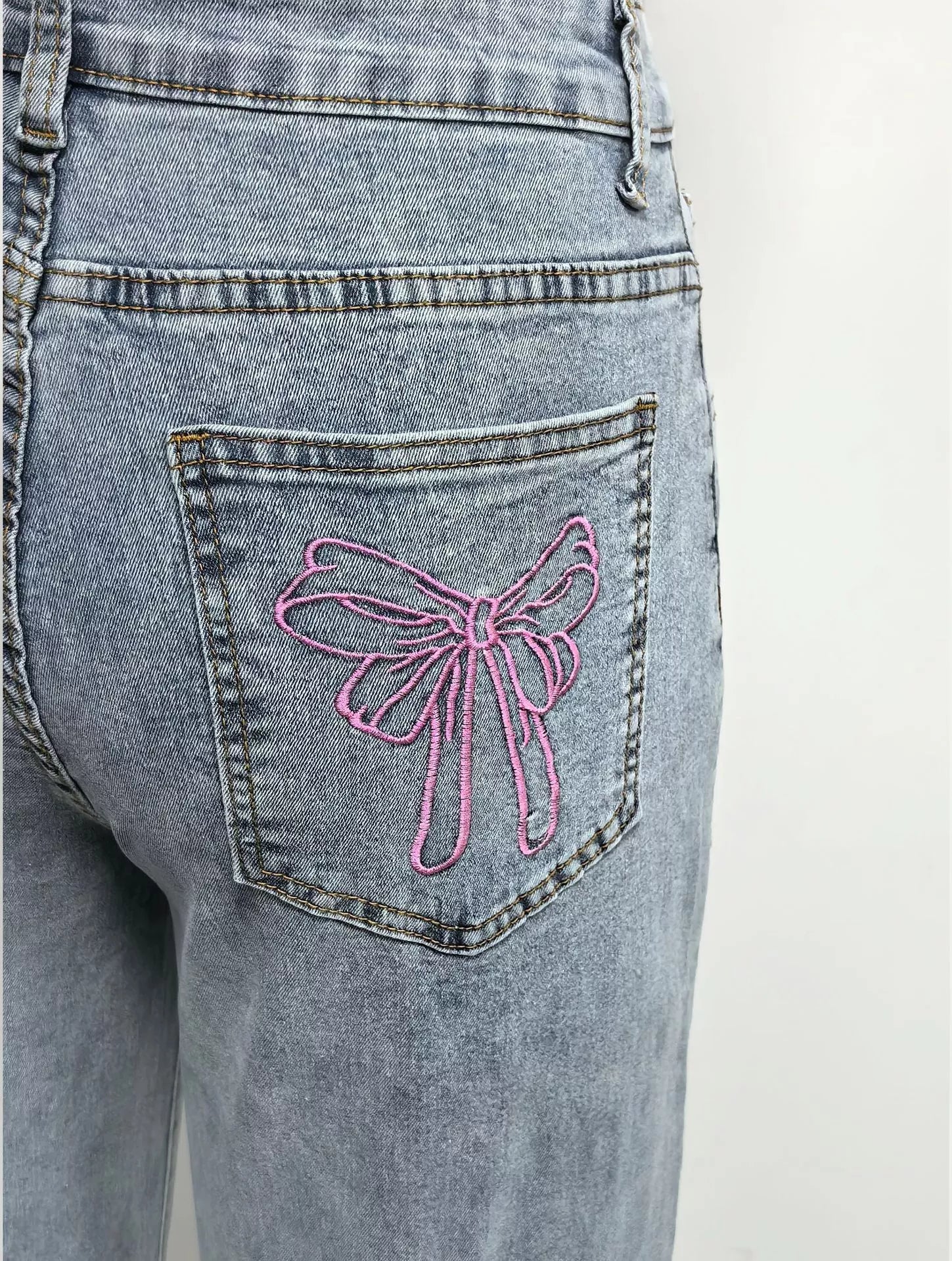Blue jeans with a pink bow design on the back pocket against a white background