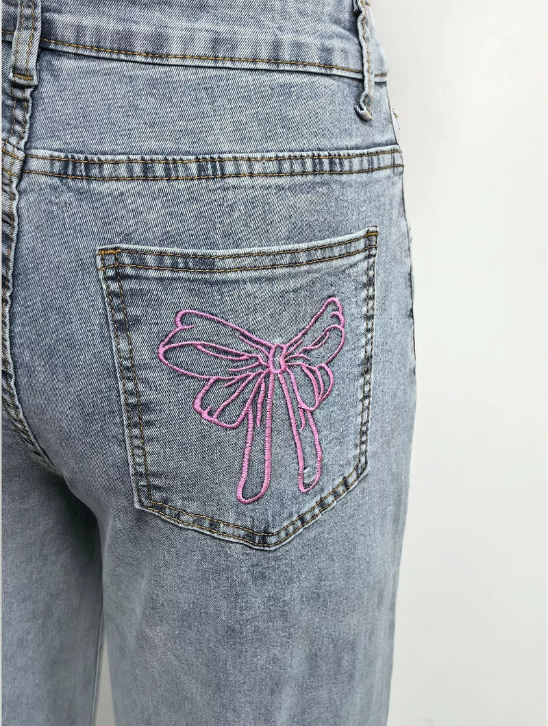 Blue jeans with a pink bow design on the back pocket against a white background