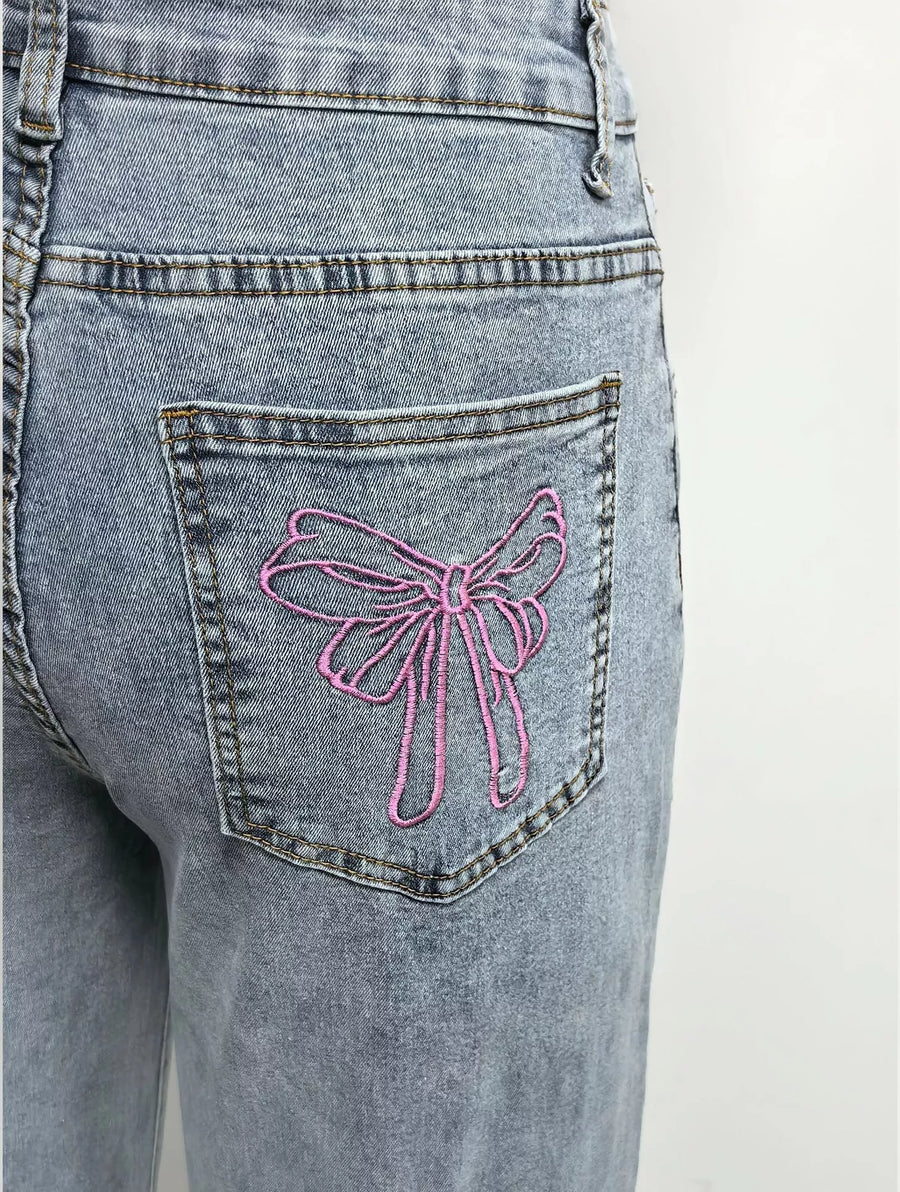 Blue jeans with a pink bow design on the back pocket against a white background