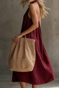 Woman in a burgundy dress holding a textured beige bag against a neutral background