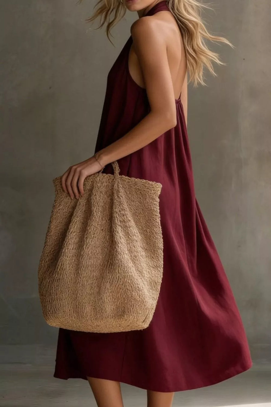 Woman in a burgundy dress holding a textured beige bag against a neutral background