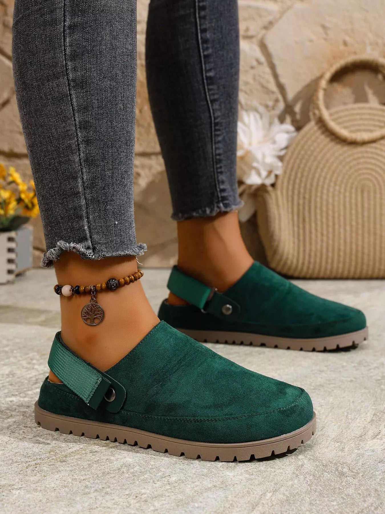 Green slip-on shoes worn with jeans on a stone surface.