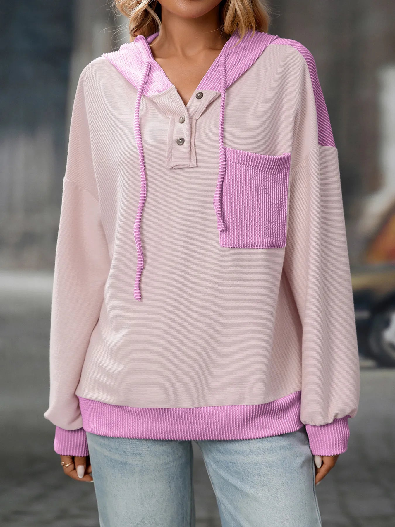 Person wearing a light pink and purple hoodie with a blurred background