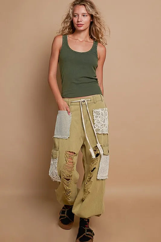 Woman wearing a green tank top and beige patchwork pants on a beige background