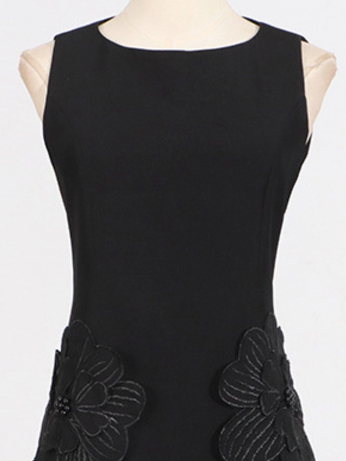 Black sleeveless dress with floral appliqués on a mannequin against a white background
