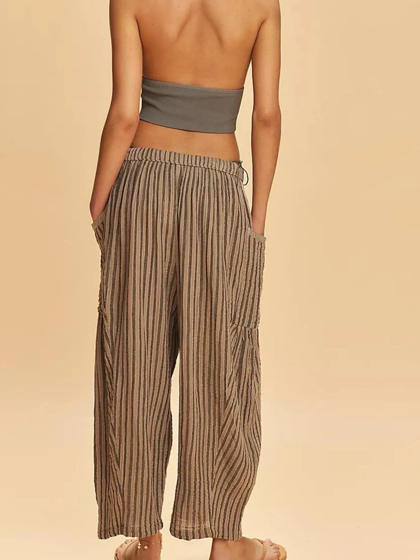 Woman wearing a strapless top and striped pants on a beige background