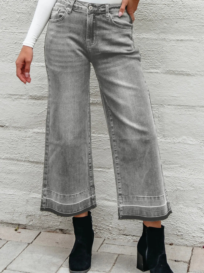 Person wearing gray wide-leg jeans against a light stone wall.